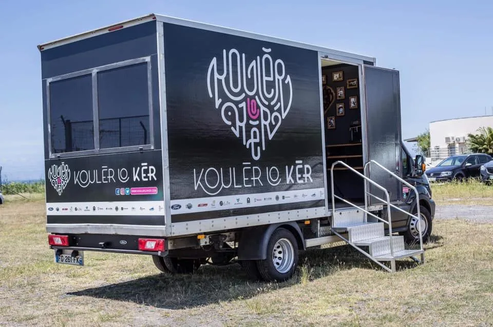 Le camion de Kouler Lo Ker, portant le nom et le logo de l’association, avec sa porte ouverte et un escalier d’accès.