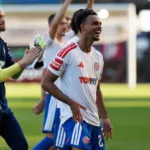 Mathieu Acapandié souriant, en tenue de Hajduk Split, sur la pelouse avec ses coéquipiers.