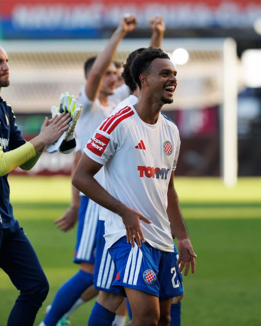 Mathieu Acapandié souriant, en tenue de Hajduk Split, sur la pelouse avec ses coéquipiers.