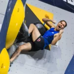 Oriane Bertone sur un bloc d’escalade à Salt Lake City, en maillot bleu, le poing levé près des prises jaunes.