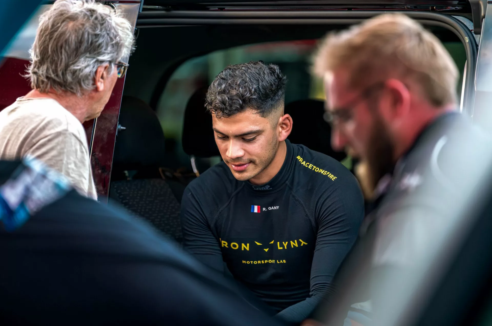 Rehane Gany en combinaison de pilote, assis au milieu de son entourage.